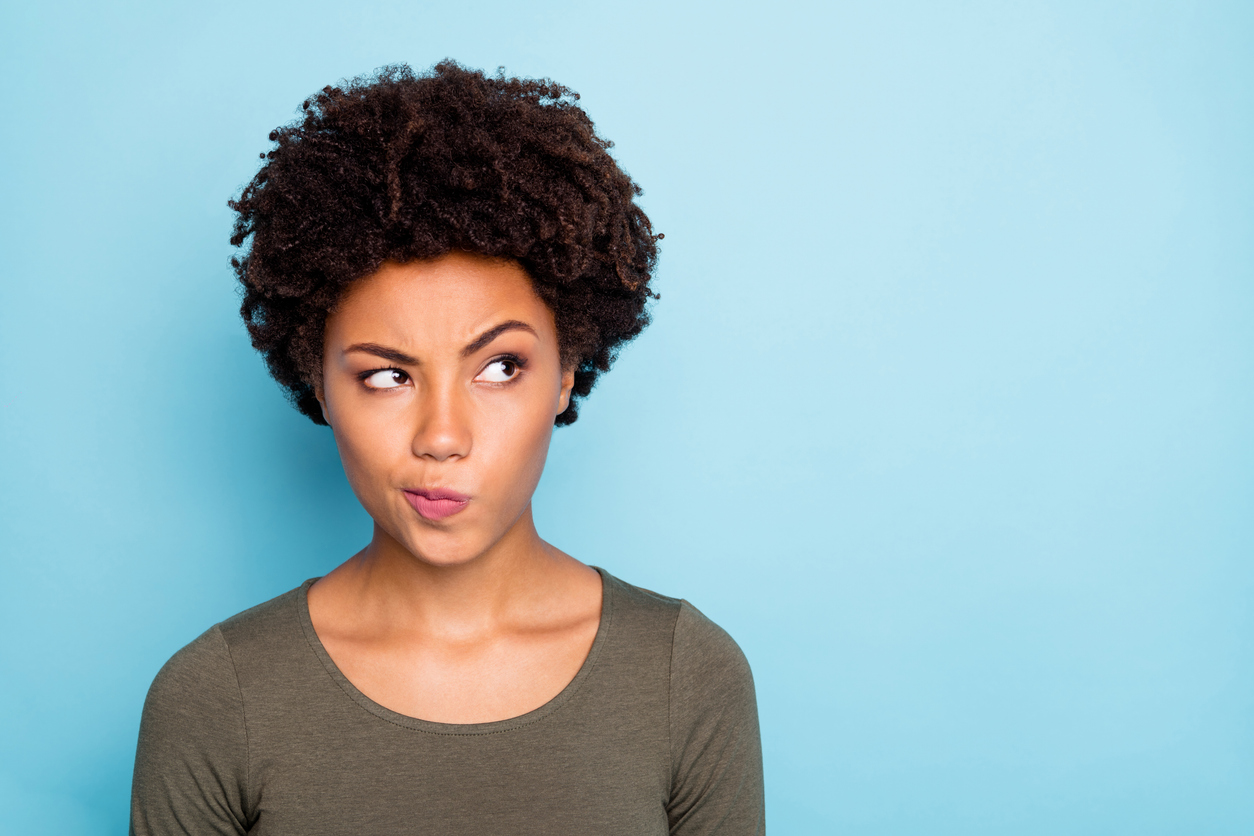 A woman with a puzzled expression deciding between DIY cleaning and hiring professional house cleaners, standing in front of a light blue backdrop
