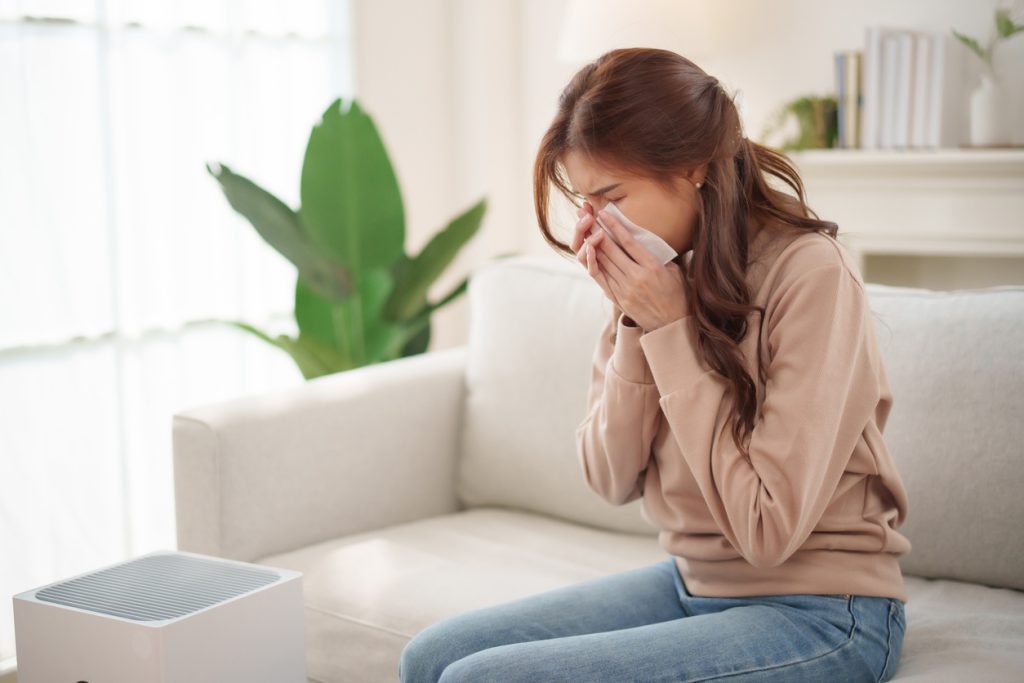 Woman sneezing in her living room due to dust and poor air quality, showing why homes can feel dusty even after cleaning.