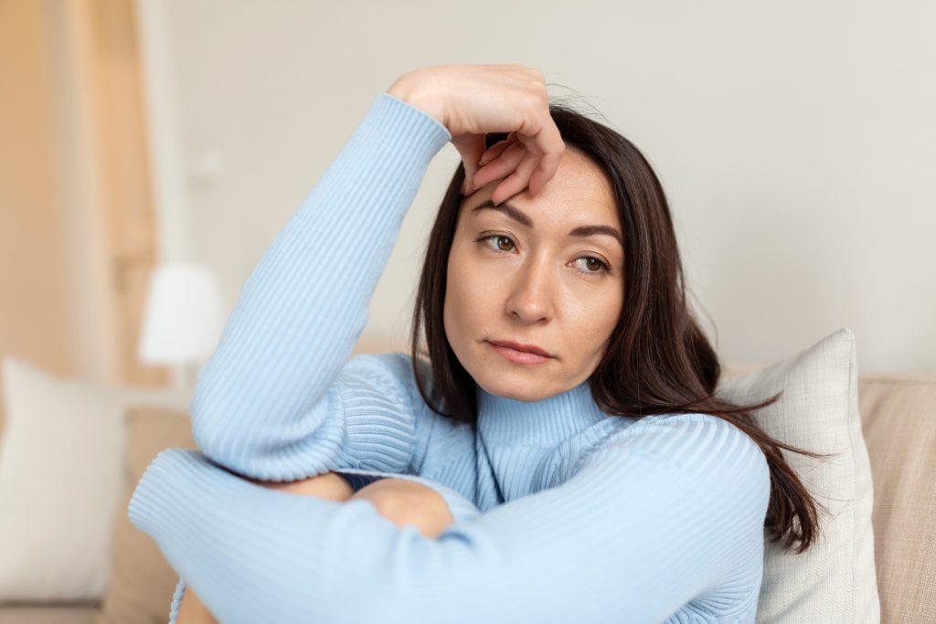 A woman sitting on a couch looking frustrated and uncertain, reflecting on whether it’s time to switch cleaning companies.