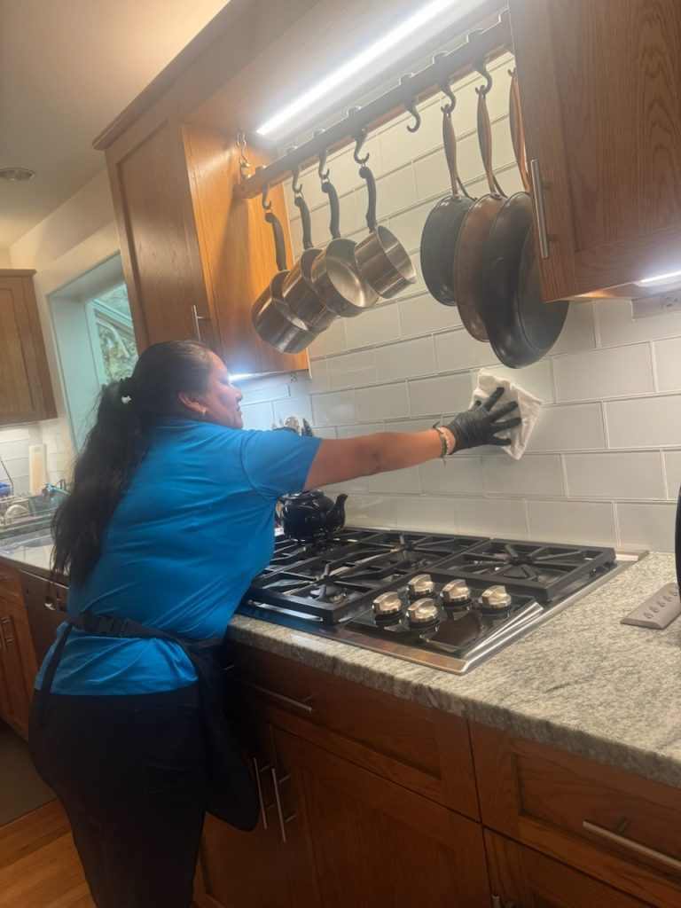 Professional cleaner performing detailed kitchen cleaning, one of the most time-consuming rooms to clean