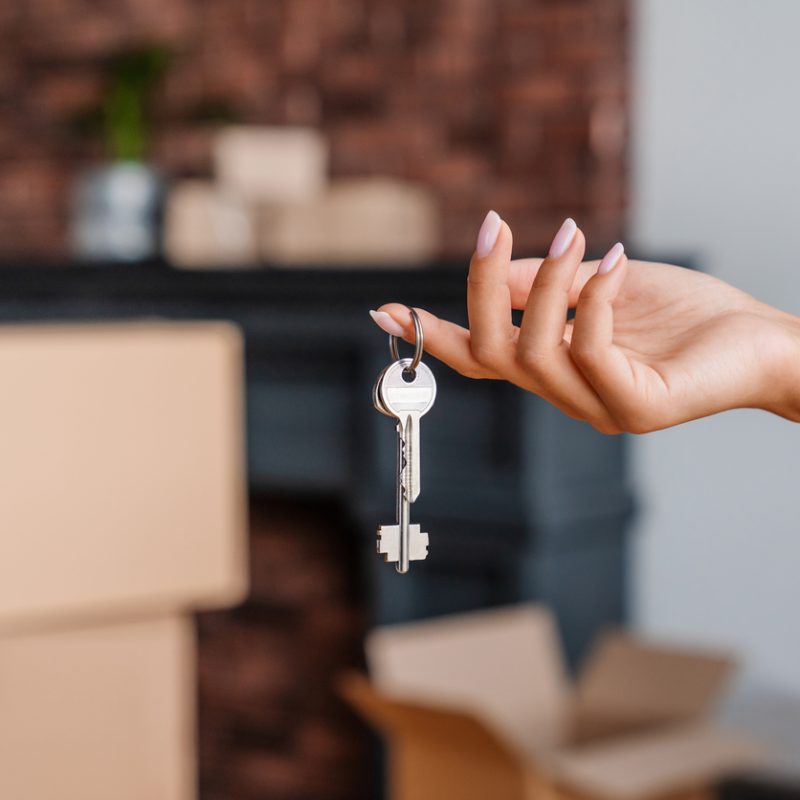 House keys in hand with moving boxes, ready for move-in or move-out cleaning