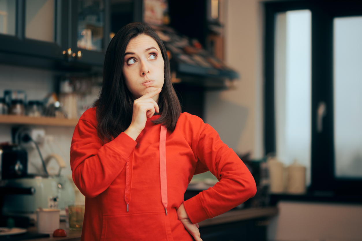 Woman in a kitchen thinking about whether she needs to clean before professional cleaners arrive