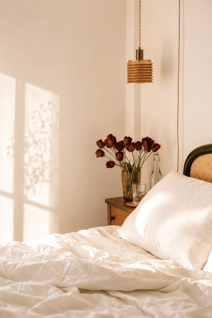 Sunlit bedroom in a clean and healthy home with soft white bedding, fresh tulips, and a calm, clean atmosphere